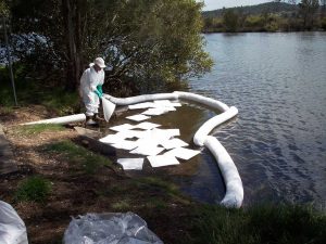 Worker using N-Fiber oil absorbent pad to clean oil spill on river
